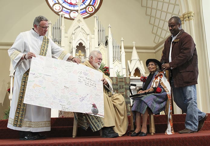 Deacon Ron Manning, standing, and Msgr. Henry Gracz, sitting, pastor of the Shrine of the Immaculate Conception, Atlanta, open up the birthday card for Emily Milner, which was signed by family, friends and members of the parish. She also received a special rosary, a photo album and a small birthday cake. Photo By Michael Alexander