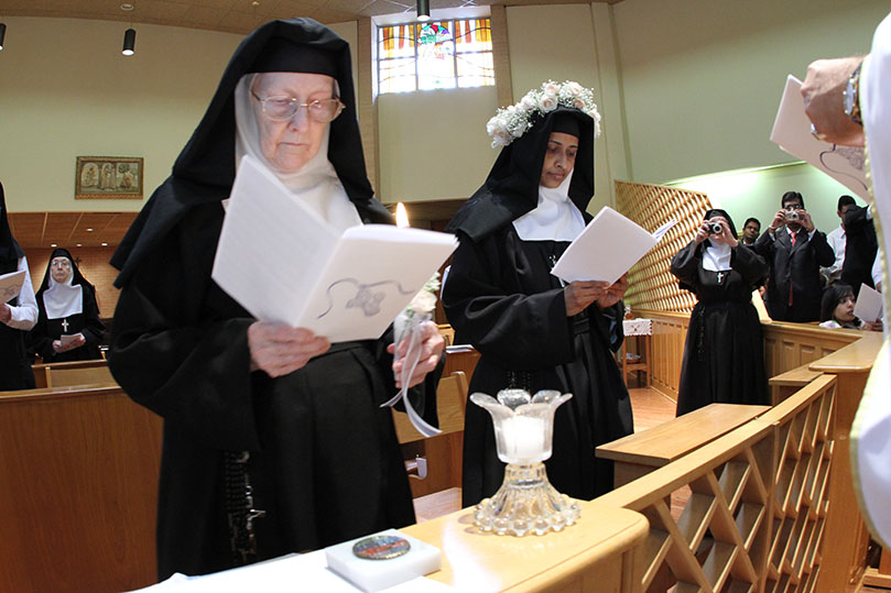 After receiving the veil and the cross, Sister Teresa Maria, right, prepares to receive the lighted candle, which symbolizes the light for her path to a life of consecrated service in the Church and her religious community. Photo By Michael Alexander  