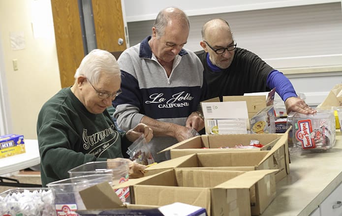 (Foreground to background) Jim Towhey, Bob DeSantis and Denis Clos pack the condiment bags, which also include cereal, coffee, grits, hot chocolate, oatmeal and other items. Photo By Michael Alexander