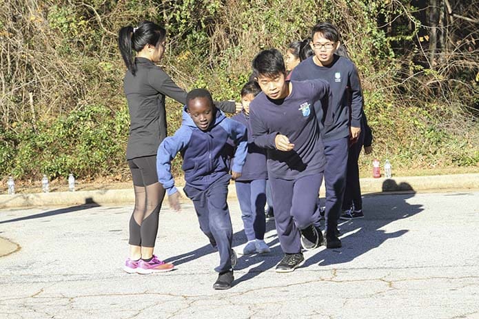 Leann Martin, far left, a third- and fourth-grade teacher at St. Peter Claver Regional School, Decatur, sends student members of the Kilometer Kids off in pairs during a warmup run through the school parking lot. Starting the run off are second-grader John Sisoun, foreground left, and seventh-grader Soe Reh, foreground right. Photo By Michael Alexander