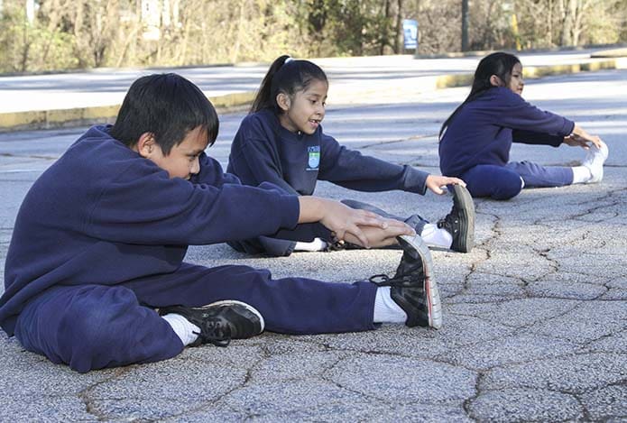 (L-r) Seventh-grader Robert Nyeing, third-grader Giovanna Miranda and second-grader Monica Khai do some group stretching exercises during a December 2017 practice of the Kilometer Kids at St. Peter Claver Regional School, Decatur. The running club is comprised of second-, third-, seventh- and eighth-graders. Photo By Michael Alexander