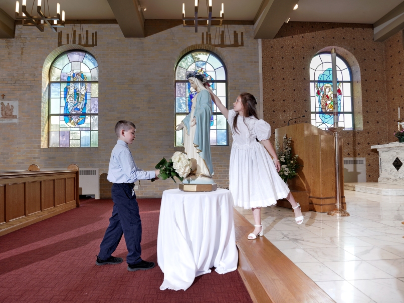 Second-grade student Charlotte Pettus, center, crowns Mary at St. Thomas More Church in Decatur. Harlan Kelso, first grader at left, brings Mary roses. Both students recently received first Eucharist. Photo by Johnathon Kelso