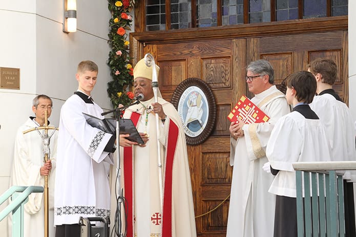 Seminarian Dan Fitzgerald holds the book as Archbishop Wilton D. Gregory faces the congregation and conducts the rite for the opening of the Holy Door of Mercy. Looking on, third from right, is Deacon Dennis Dorner, Archdiocese of Atlanta chancellor. Photo by Michael Alexander