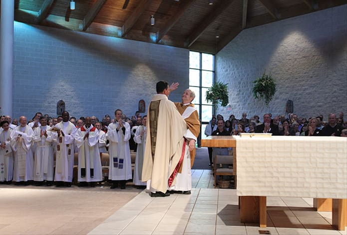 Msgr. Patrick Bishop, standing right, welcomes his replacement, Father Fernando Molina Restrepo, to the altar where he gives his brother priest a “high five” before the congregation. Photo By Michael Alexander