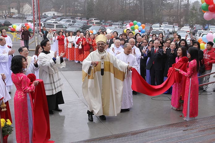 Archbishop Wilton D. Gregory, center, smiles and the congregation applauds after he cuts the ribbon at the bottom of the steps leading to Our Lady of Vietnam Churchâs new worship space. Photo By Michael Alexander