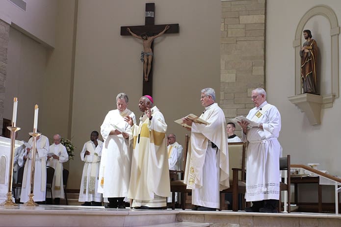 Archbishop Wilton D. Gregory conducts the prayer of dedication as Deacon Victor Taylor holds the prayer book. Father Larry Niese, second from the right, pastor of St. Michael the Archangel Church, and Deacon Taylor built the cross on the wall behind them. The corpus of Jesus came from Italy. Photo By Michael Alexander