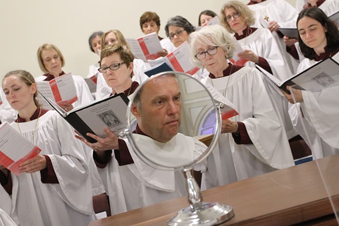 Music director and organist Mike Ostro is reflected in the mirror on top of his organ as the choir sings âAve Verum,â under the direction of Nila Alexander. The choir loft has built in risers and the new practice room has amenities like a rack for choir robes, music cubbies and storage space. Photo By Michael Alexander