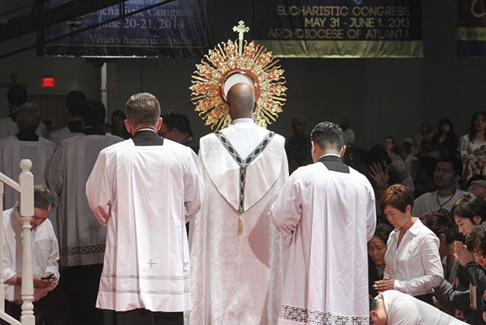 Escorted by Deacon Gary Schantz, left, of St. Andrew Church, Roswell, and Father Rey Pineda, right, parochial vicar at Saint Lawrence Church, Lawrenceville, Father Desmond Drummer, center, parochial vicar at St. Peter Chanel Church, Roswell, removes the monstrance containing the Blessed Sacrament from the exhibit hall. Photo By Michael Alexander