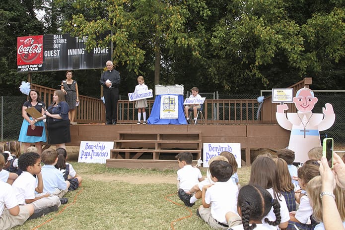 (Standing, ground level, l-r) Computer teacher Katrina Poff and music teacher Allison Carter sing âMake Me a Channel of Your Peaceâ during a symbolic welcome of the pope to the United States. Listening and looking along with the students, parents and members of the community are (on the platform, l-r) director of Faith Formation Carmen Graciaa, Immaculate Heart of Mary Church pastor Msgr. Albert Jowdy, fourth-grader Grace Sheehy and her brother Will, a third-grader. Photo By Michael Alexander