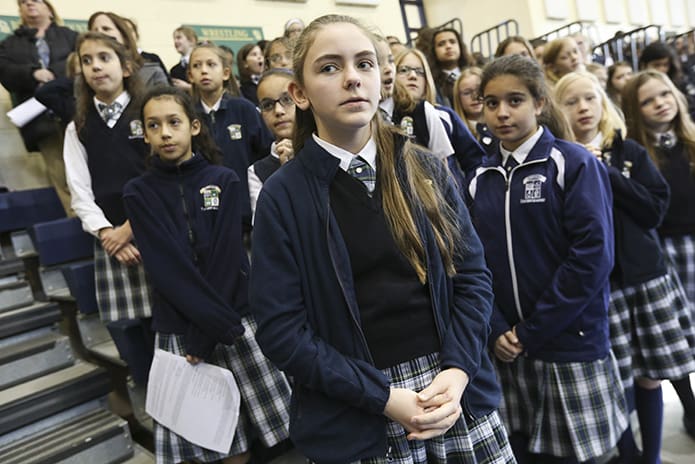 Pinecrest Academy’s Sydney Cobak, center, stands with fellow fifth-graders during the praying of the Our Father. They were on hand for the Feb. 2 Founder’s Day Mass in the school gymnasium. Photo By Michael Alexander