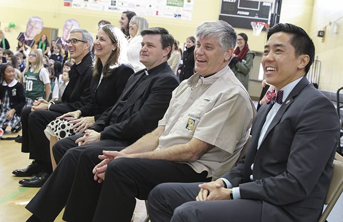 (R-l) John Huynh, instructional technology coordinator, Bishop Bernard E. Shlesinger III, Legionaries of Christ Father David Steffy, school president, Kathleen Nichols, formation director, and Legionaries of Christ Father Matthew A. Kaderabek, lower school chaplain, enjoy the lower school pep rally as it unfolds. Familiar with Bishop Shlesinger’s affinity for fishing, the lower school presented him with a Pinecrest Academy fishing shirt. Photo By Michael Alexander