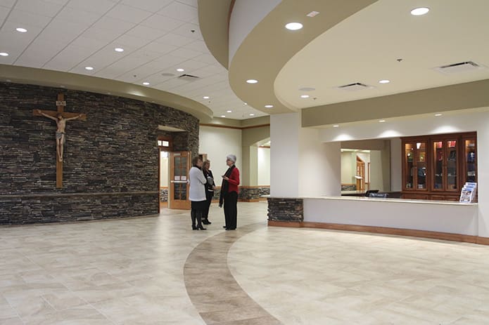 (L-r) Joanie Chenier, parish finance manager, Adela Achtman, parish receptionist, and Lelis Knight, assistant to the priests, gather in refurbished narthex between the new day chapel exterior, left, and the new parish store. The new narthex was created by rearranging former offices, confessionals and storage space. Photo By Michael Alexander