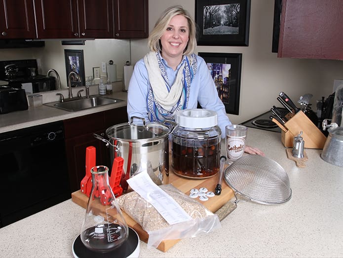 Sarah Vabulas, 31, stands among some of her home brewing supplies and beer in her Atlanta apartment. In 2015 Vabulas, a member of the Cathedral of Christ the King, published her book, “The Catholic Drinkie’s Guide to Homebrewed Evangelism.” Photo By Michael Alexander