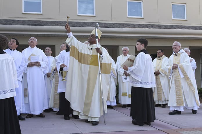 Archbishop Wilton D. Gregory, center, blesses the 74-foot-tall steeple as some of the clergy and altar servers look skyward. Photo By Michael Alexander