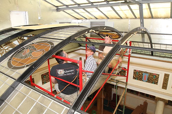 From the highest point on their 16 foot scaffold (front to back) Frank Llorens Jr., Frank Sr. and Robert Zortea make final preparations before they start installing the final 16 glass panels of the refurbished vaulted glass skylight at St. John Chrysostom Melkite Catholic Church, Atlanta. The Llorens are the proprietors of Llorens Leaded Art Glass, Inc., Winder, which dates back to 1912. Frank Sr.’s father, Joseph Victor, was the original designer of the vaulted glass ceiling when it was the mansion of the late Coca Cola mogul Asa Candler. Photo By Michael Alexander