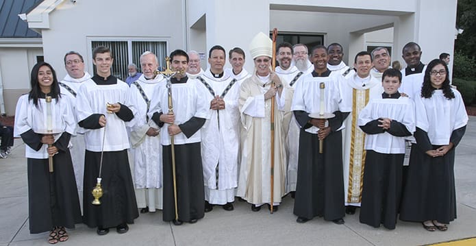 Clergy and altar servers join St. Theresa of the Child Jesus Church pastor Father JesÃºs David Trujillo-Luna, fifth from the right, and main celebrant Bishop Luis Zarama, right center, for a group photo after the 30th anniversary liturgy. Two former pastors, Father Richard Tibbetts, retired, fourth from the left, and Father Fernando Molina-Restrepo, pastor of Transfiguration Church, Marietta, left center, were also on hand. Photo By Michael Alexander