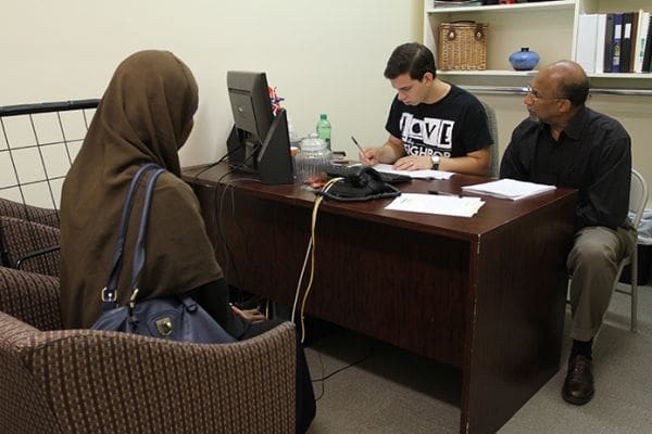 St. Vincent de Paul caseworker Daniel Jones, background left, looks over the paperwork of a client as volunteer Ben Davie, background right, looks on. Photo By Michael Alexander