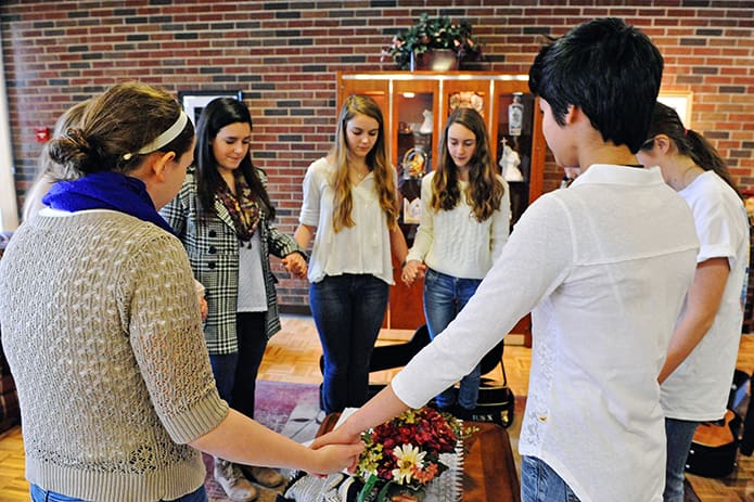 High school student members of Teens Reaching Out Through Tunes (TROTT) pray before they begin their performance for patients at Our Lady of Perpetual Help Home on Jan. 31.  Clockwise from left are: Grace Garrett, 17; Caroline Holt, 16 (hidden); Maggie Weir, 16; Caroline Tanzy, 17; Mary Margaret Cozart, 14; Sam Repasky, 14 (hidden) ; Grace Repasky, 14; and Michaela Pocock, 17.  All attend St. Pius X High School except Michaela Pocock, who is from Roswell High School. Photo By Lee Depkin