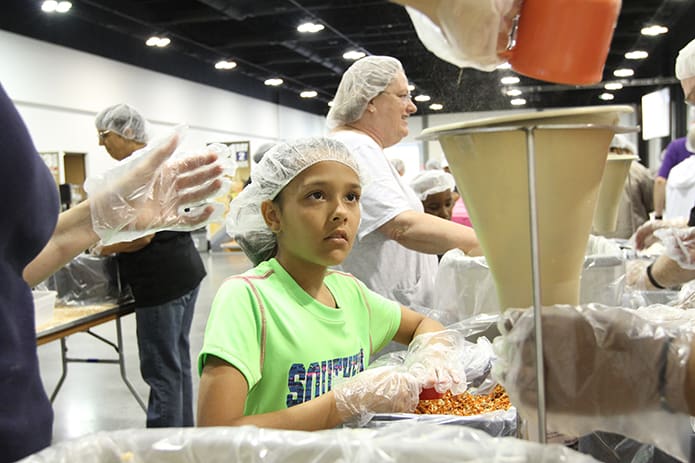 Ten-year-old Amelia Taglieri watches her mother, Jennifer, pour the final contents of soy into a funnel as another volunteer holds the meal bag under it. Amelia had the job of adding dehydrated vegetables to the meal bag. The mother and daughter belong to St. Lawrence Church, Lawrenceville. Volunteers packed 100,000 meals for Burkina Faso, West Africa, June 16. Photo By Michael Alexander