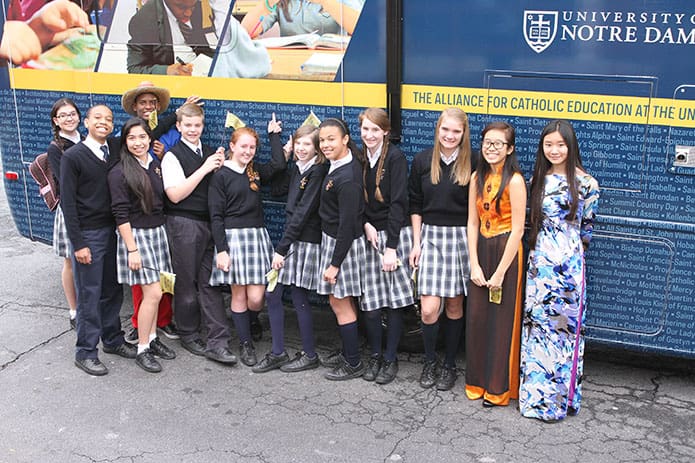 St. John the Evangelist eighth grade ambassadors stand by the University of Notre Dameâs Alliance for Catholic Education national tour bus as some point to their schoolâs name. The name of every Catholic school in the country is printed on both sides of the bus. Photo By Michael Alexander