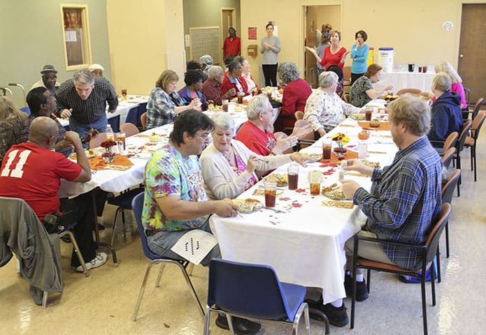 After a group dinner blessing, Cathy Clutter, background standing, second from right, welcomes and invites the participants to eat up and enjoy the meal. While Clutter and her family have volunteered for more than a decade, this is the third year she has coordinated the annual Denney Tower Thanksgiving dinner for the University of Georgia Catholic Center. Photo By Michael Alexander