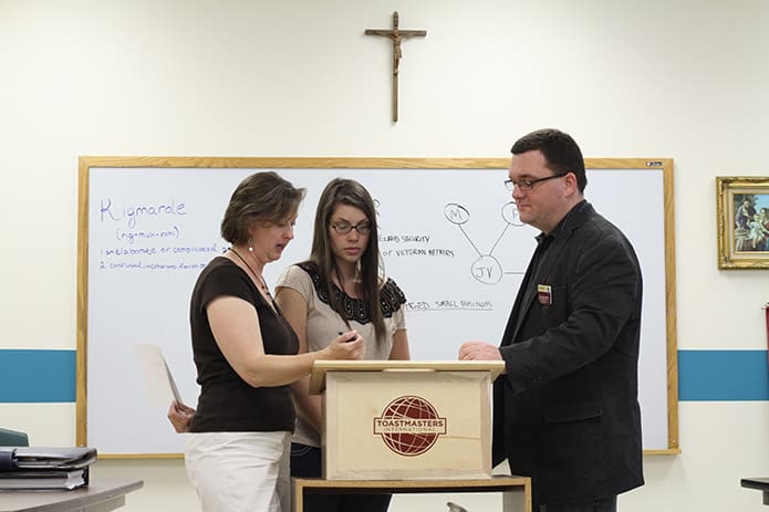 Meghan Riley, left, and John Hartwell, right, discuss the protocol for acting in the role of âtoastmaster of the dayâ with Kelly Akin, a yearlong member of the YAM Toastmasters Club. Riley has been affiliated with the club for three years. Hartwell is one of the clubâs founding members and the immediate past president. Photo By Michael Alexander