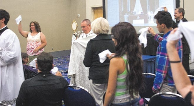 Bishop David Talley, center, exits the American Sign Language track with the Blessed Sacrament as attendees wave white handkerchiefs symbolizing their love for Jesus.