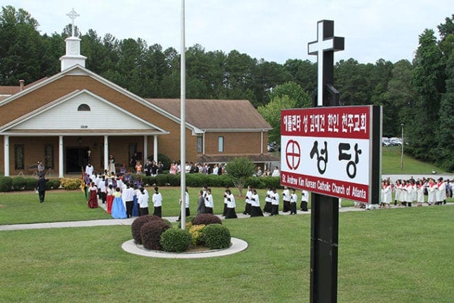 Led by a group of altar servers carrying a relic of St. Andrew Kim, the pastor and congregation approach the church for the 10 a.m. Sunday Mass. Photo By Michael Alexander