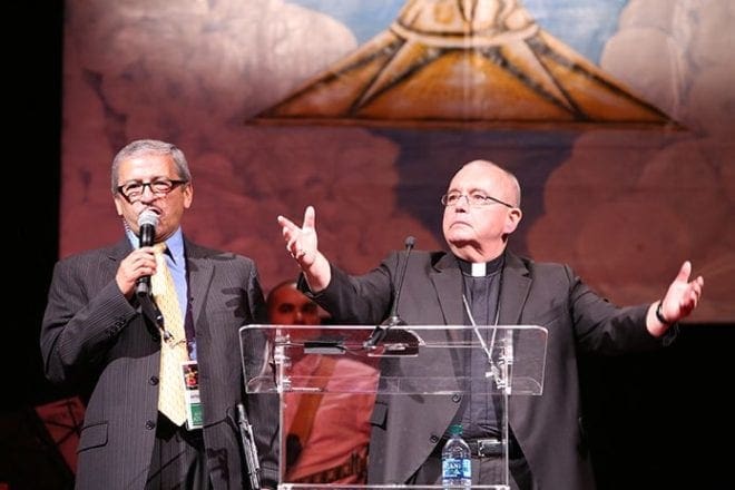 At one point during a visit to the Spanish track Bishop David P. Talley, right, rallied the crowd by having them chant in unison “Construir puentes, no muros (Build bridges, not walls).” Standing next to him at the podium is Jairo Martinez, archdiocesan director of Intercultural and Ethnic Diversity. Photo By Michael Alexander