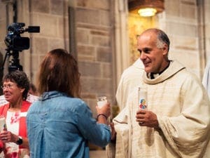 Legionary of Christ Father Juan Guerra presents a candle with the likeness of St. Pope John Paul II to a pilgrim. The candles will be used by friends and family members for prayer while the youth are away. Photo By Joseph Pham